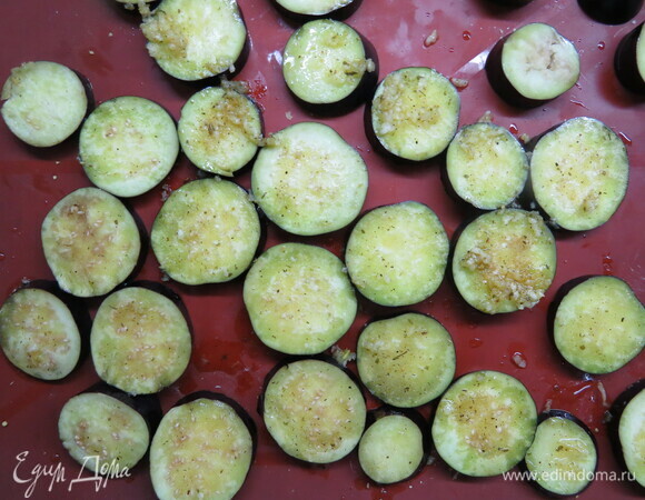 Баклажаны нарезать кружочками толщиной 0,4–0,5 см, выложить на противень (я выкладывала на силиконовый коврик), смазать чесночным маслом с помощью кулинарной кисти и запекать в духовке 25–30 минут при 180°C.