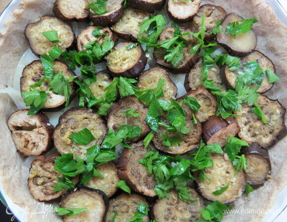 На подпеченную основу выложить сначала лук, потом слой баклажанов, сверху залить яичной смесью. Поставить пирог в духовку, выпекать 35–40 минут.