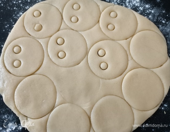 Разделить тесто на две части. Одну часть теста раскатать в пласт толщиной где-то 0,5 см. С помощью круглой формы или стакана вырезать четное количество кружков. Половину кружков оставить целыми, а в остальных вырезать глазки.