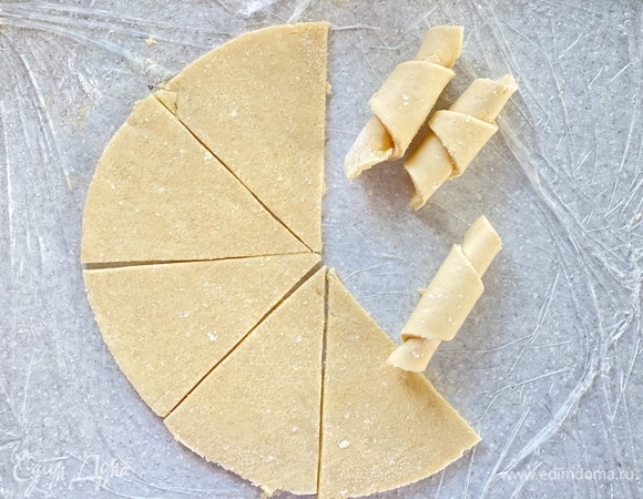 Раскатать в пласт толщиной 0,3 см. Вырезать ровный круг при помощи тарелки. Посыпать сахаром и разрезать его на восемь равных частей. Скрутить каждую часть в рогалик. Окунуть заготовки в сахар и выложить на противень.