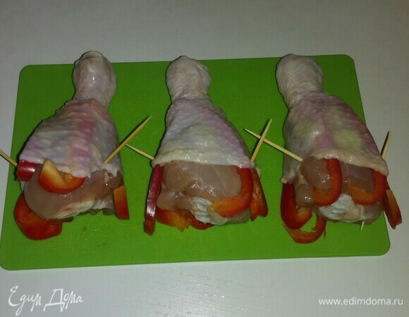 Кладем на каждую куриную голень нарезанный чеснок и полоски болгарского перца. Затем опускаем на чеснок и болгарский перец кожу и закрепляем ее зубочистками.