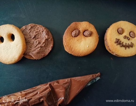 Готовим крем. Растопить шоколад на водяной бане, половину шоколада смешать с рикоттой. Вторую половину переложить в кондитерский мешок. Далее взять круглое цельное печенье, выложить на него немного крема и накрыть печеньем с отверстиями для глаз, немного надавить. Затем шоколадом нарисовать нос и рот. В результате получаются немного смешные, немного страшные и в то же время забавные смайлики.