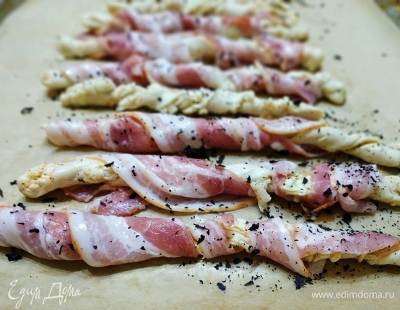 Каждый жгутик обмотать полоской бекона и посыпать сухими травами по вкусу. У меня — сушеный базилик. Выпекать 15–20 минут при 180°C.
