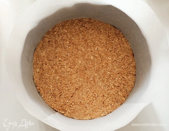 Печенье и орехи измельчить, добавить 1/2 ч. л. мускатного ореха и растопленное сливочное масла. Перемешать. Разъемную форму для выпечки застелить пергаментной бумагой. На дно формы выложить печенье, распределить и утрамбовать. Поставить форму в холодильник.