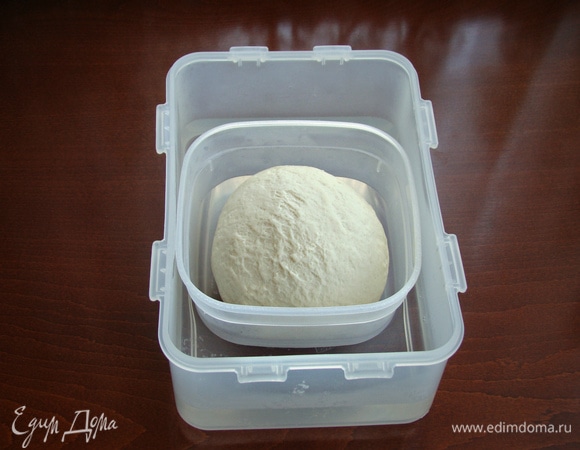 После этого тесто хорошо вымешивать в течение 10 минут. Оно не липнет к рукам. После тщательного вымешивания поместить тесто в небольшую емкость, накрыть плотно крышкой и поставить в большую по размеру емкость. В нее налить горячей воды и оставить прогреваться тесто на 30 минут.