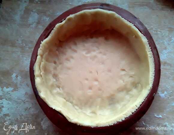 Затем достать тесто из холодильника, раскатать на доске. Его должно хватить на форму диаметром 21 см. Необходимо, чтобы края свешивались с формы. Потом их аккуратно срезаем на уровне бортиков. Хорошо прижимаем тесто к форме и помещаем на противень.