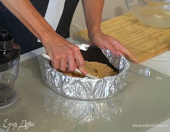 Разъемную форму для выпекания внутри застелить пергаментом, а снаружи обернуть несколькими слоями фольги, на дно формы равномерно выложить печенье с маслом и убрать в холодильник.