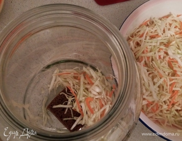 На дно пятилитровой банки кладем кусочек хлеба. Его можно прикрыть капустным листом, а можно не прикрывать, а сразу выкладывать в банку капусту и плотно утрамбовать кулаком до появления сока.