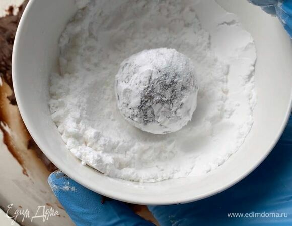 В миску насыпьте примерно 50 г сахарной пудры и обваляйте в ней каждый шарик. Сахарную пудру не стряхивайте — так печенье получится более красивым.