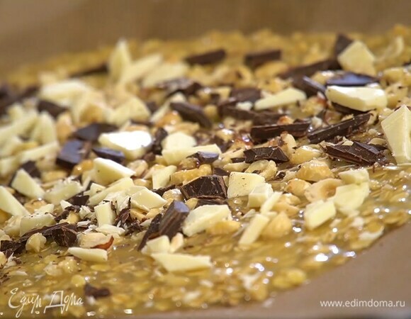 Вылить тесто на противень, застеленный бумагой для выпечки, разровнять в тонкий пласт и посыпать сверху измельченными орехами и шоколадом.