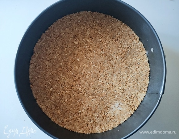 Измельчить печенье, добавить растопленное сливочное масло, перемешать. Форму для запекания застелить пергаментной бумагой. Выложить печенье, утрамбовать и убрать форму в холодильник.