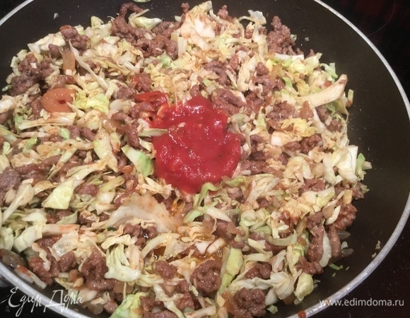 Добавьте нашинкованную капусту, томатную пасту, сахар, перемешайте и тушите на медленном огне, пока вся жидкость не испарится.