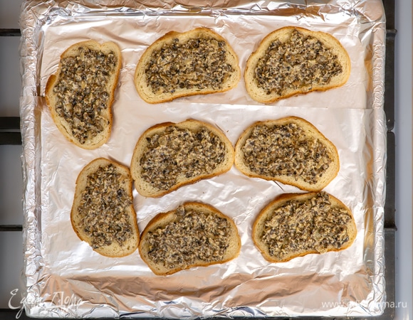 Противень застелить фольгой и равномерно разместить на нем ломтики батона. Выложить приготовленную грибную начинку на каждый кусочек хлеба, посыпать сверху оставшимся сыром.