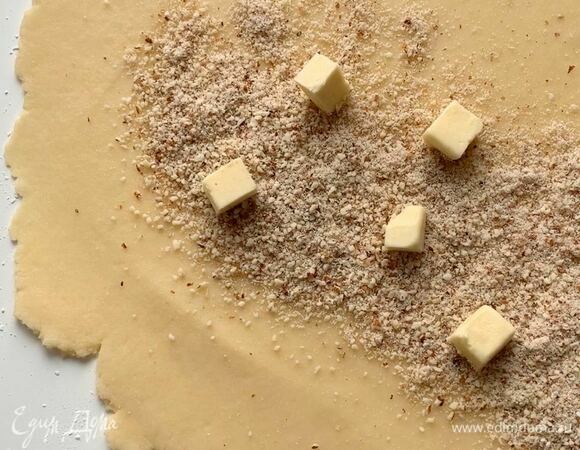 Достаньте тесто из холодильника, раскатайте толщиной 5–6 мм. По короткому краю посыпьте миндальной крошкой (бороздку толщиной 5 см), сверху выложите кубики сливочного масла.