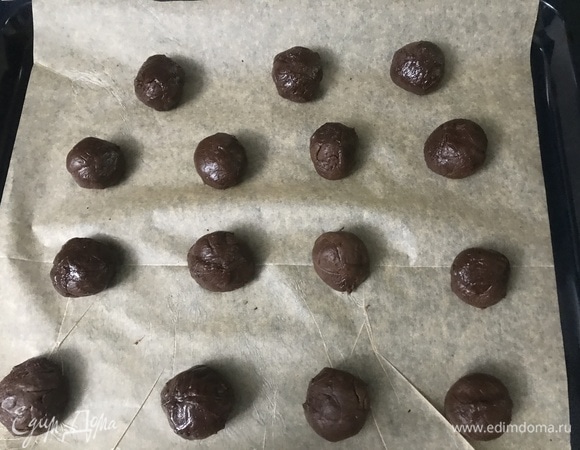 Сливочное масло жирностью 82,5 % взбить с сахаром до воздушной светлой массы. Не переставая взбивать, добавить по одному яйца (некрупные, у меня С2). Темный шоколад (54 %) растопить на водяной бане до температуры не выше 35°C. Добавить шоколад к масляной смеси и еще раз взбить. Муку, какао и разрыхлитель перемешать, просеять. Добавить мучную смесь к шоколадной и хорошо вымешать тесто. Консистенция будет жидковатой. Накрыть тесто пленкой и убрать в холодильник на час. Духовку разогреть до 170°C. Слепить из теста шарики (удобнее будет работать в перчатках) и разложить на застеленный пергаментом противень на расстоянии друг от друга.