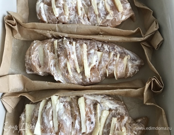 Чеснок очистить, измельчить. Для соуса смешать сметану или майонез с измельченным чесноком, можно добавить немного мелко рубленой зелени (по вкусу). Сыр нарезать пластинками толщиной 2 мм (по размеру прорезей). Из плотного пергамента (у меня силиконизированный) сделать лодочки: вырезать прямоугольники и завернуть со всех сторон. Для каждой грудки — своя лодочка. Не выпекайте на фольге: низ будет пригорать, грудка будет сухой. А пергамент сохранит весь сок. Каждую грудку приправить специями, хорошо смазать соусом (в том числе все разрезы) и вставить в каждый разрез по кусочку сыра.