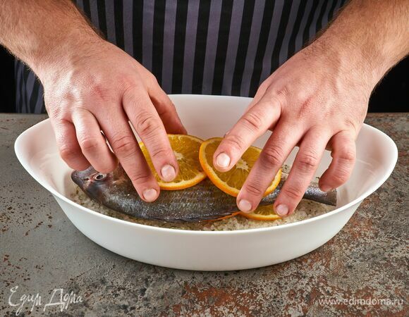 На соль уложите рыбу целиком, сверху — дольки апельсина.