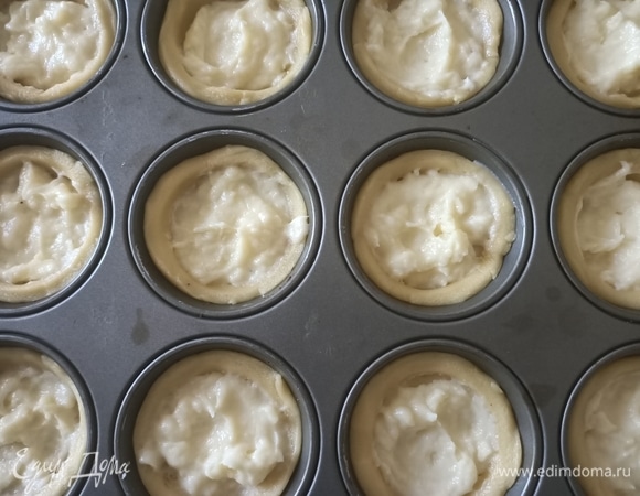 Форму для маффинов смазать маслом и посыпать мукой. Поместить бумажные формочки в форму. В центр выложить немного крема.