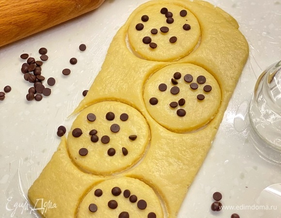 По истечении времени тесто раскатать в пласт толщиной 1 см и вырезать круги. Сверху посыпать шоколадными каплями или шоколадом. Немного вдавить в тесто. Выпекать на пергаменте 15–20 минут (до румяности) при 185°C.