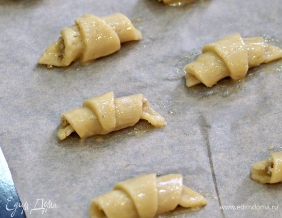 Духовку разогреть до 180°C. Выложить рогалики на противень, застеленный пергаментом. Смазать желтком.