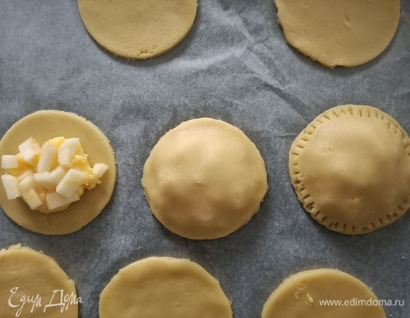 Достать тесто из холодильника. Раскатать и вырезать круглые заготовки. В центр круга выложить немного крема, сверху положить яблоки и накрыть тестом. Закрепить края с помощью вилки.