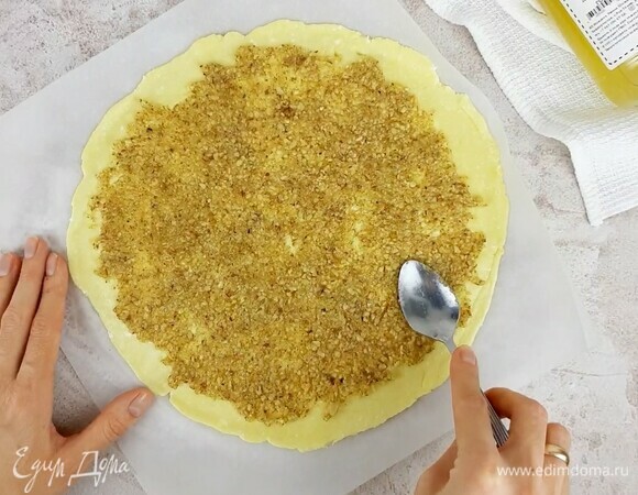 Достаем одну часть теста из холодильника и раскатываем между двумя листами пергамента. Формируем круг диаметром 25 см. Равномерно распределяем половину ореховой начинки.