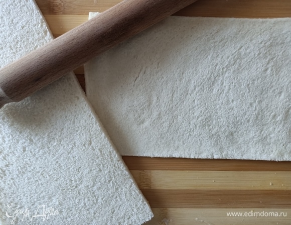 С хлеба срезать корку. Уложить два кусочка хлеба рядом на разделочную доску, сделать нахлест размером 1 см так, чтобы из двух квадратов получился один прямоугольник. Раскатать хлеб скалкой. Нам понадобится два таких прямоугольника.