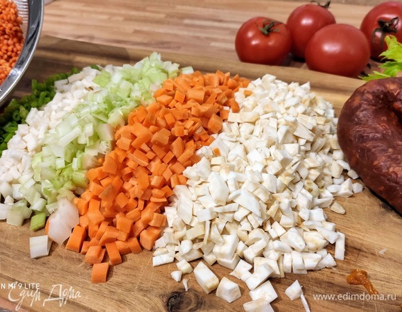Очистите лук, морковь, корень петрушки, оба вида сельдерея, кусочек перца чили и нарежьте мелкими кубиками размером с чечевицу. Использовать ли перец чили — решайте сами. Чаще всего колбаски чоризо уже достаточно острые, поэтому остроту регулируйте по своему вкусу. В большой кастрюле разогрейте сливочное и оливковое масло и обжарьте лук на медленном огне. Я нашинковала стебли петрушки и добавила их к овощам. Также можно использовать пастернак и/или любой другой из корешковых овощей.