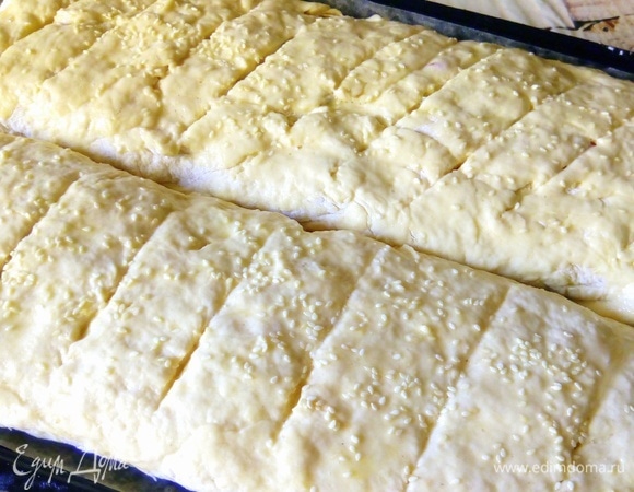 Выкладываем батоны на противень, застеленный пергаментной бумагой. Сверху делаем надрезы ножом. Смазываем батоны взбитым яйцом, посыпаем сверху кунжутом.