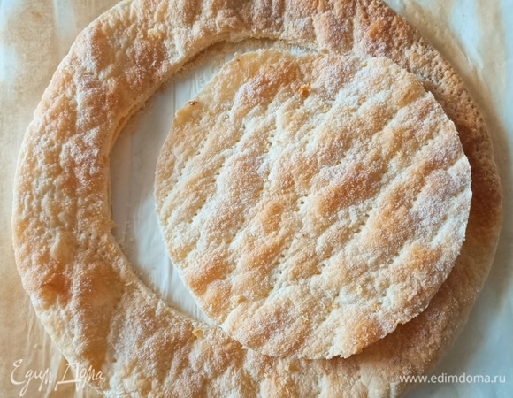 Пока выпекается бисквит, развернуть готовое слоеное тесто, наколоть его вилкой, посыпать сахарной пудрой. Выпекать в разогретой духовке при температуре 180°C в течение 12–15 минут. Готовый слоеный корж остудить, затем приложить форму, в которой выпекался бисквит, и вырезать круг. Остатки измельчить в крошку.