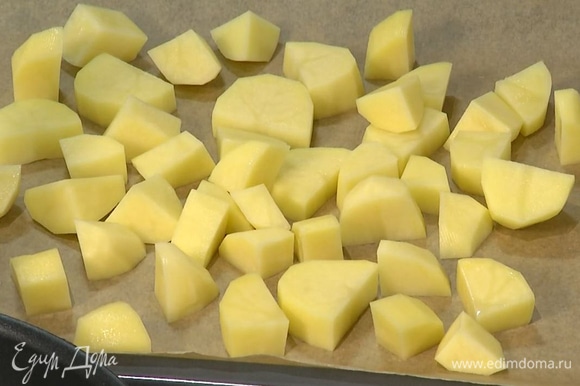 Картофель почистить и нарезать крупными брусочками, затем выложить на застеленный бумагой для выпечки противень и запекать в разогретой духовке 15–18 минут, практически до готовности.