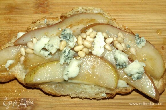 Выкладываем груши на круассан с сыром, сверху посыпаем кедровыми орехами, остатками сыра и добавляем веточки руколы.