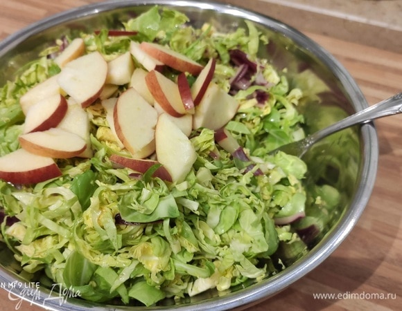 Свежую брюссельскую капусту тщательно промыть, удалить верхние грубые, возможно, испорченные листья. Разрезать пополам и тонко нашинковать. Добавить нарезанное на ломтики яблоко.