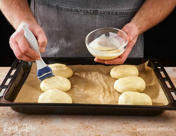 Противень застелите бумагой для выпечки, положите заготовки на небольшом расстоянии друг от друга. Смешайте яичный желток со сливками, смажьте заготовки и оставьте их в теплом месте на 40 минут на расстойку.<br />
Выпекайте булочки в предварительно разогретой до 190–200°С духовке в течение 25 минут до румяной корочки.