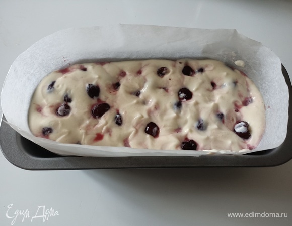 Форму для кексов застелить пергаментной бумагой, выложить тесто. Сверху уложить черешню и аккуратно обратной стороной ложки погрузить ее в тесто.