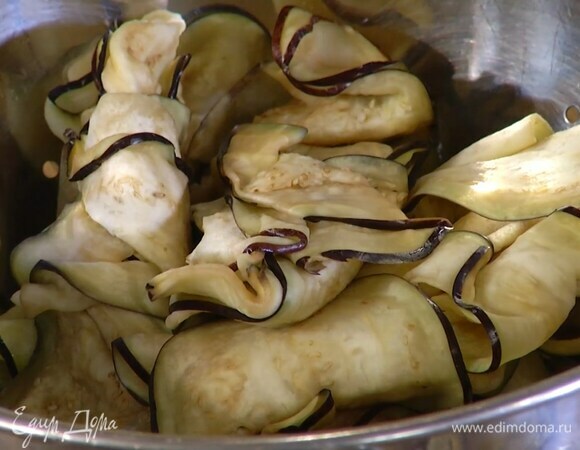 Баклажаны нарезать вдоль тонкими пластинками, выложить в дуршлаг, посолить и дать постоять 20–30 мин., затем промыть холодной водой и просушить бумажным полотенцем.