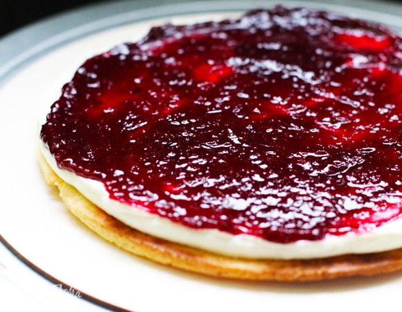 Собрать торт в кольце или просто на подложке. Я перекладываю крем в мешок и выдавливаю одинаковое количество на каждый корж. Собираем с конфи через слой. Делаем в такой последовательности: корж, крем, конфи, последний у нас — просто корж. Если корж сломается при сборке, это не страшно, укладываем встык куски, потом он пропитается, и место разлома будет незаметно.