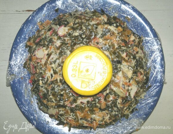 Края плоского блюда застелить пищевой пленкой. В центр блюда поставить стакан. Салат выложить вокруг стакана в форме кольца, слегка утрамбовывая.