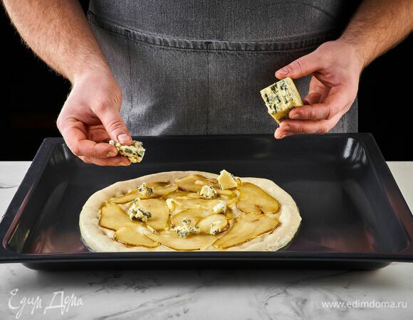 Выложите на тесто карамелизированную грушу. Сверху — кусочки горгонзолы. Выпекайте пиццу в разогретой до 250°C духовке 12–15 минут.