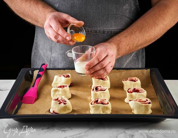 Разрежьте на порционные кусочки по 4–5 см. Выложите завитки на противень, застеленный бумагой для выпечки. Желток перемешайте с молоком, смажьте завитки и выпекайте в разогретой до 190°С духовке 17 минут.