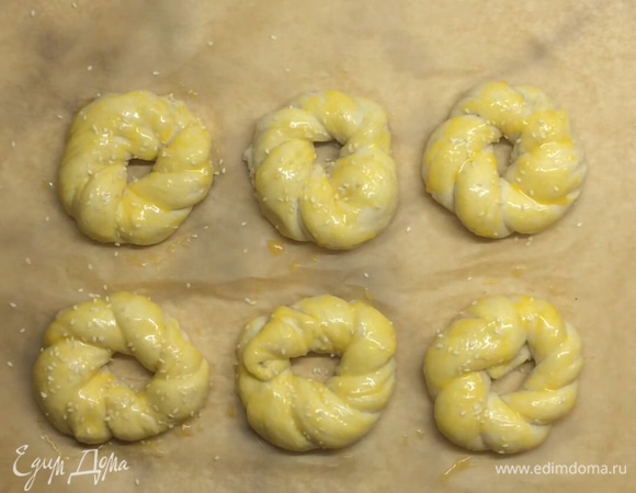 Выкладываем на противень, застеленный пергаментом, накрываем полотенцем и оставляем на 30 минут. Булочки поднимутся и станут очень воздушными. Каждую смазываем сверху желтком и посыпаем кунжутом.Отравляем в заранее разогретую духовку на 25–30 минут при 180–190°C.