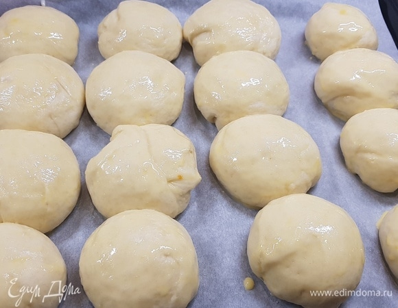 Тесто разделить на 16 кусочков. Шарик размять в небольшую лепешку, края подоткнуть к центру и залепить. Перевернуть заготовку и провернуть ее вокруг своей оси несколько раз, чтобы закрепить шов. Булочки выложить на противень, накрыть полотенцем и оставить на 30–40 минут. Смазать их яичным желтком и выпекать 20 минут при температуре 200°C.