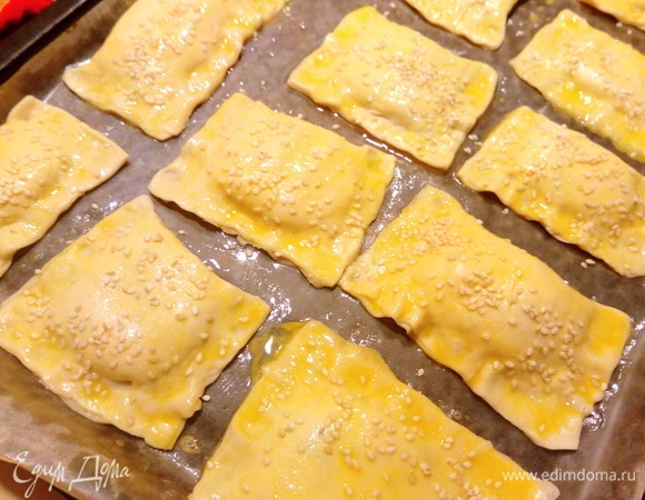 Слойки выкладываем на противень, застеленный пергаментной бумагой. Взбиваем яйцо, смазываем слойки и посыпаем кунжутом. Отправляем в духовку при 190°C на 30–40 минут, ориентируйтесь на свою духовку.