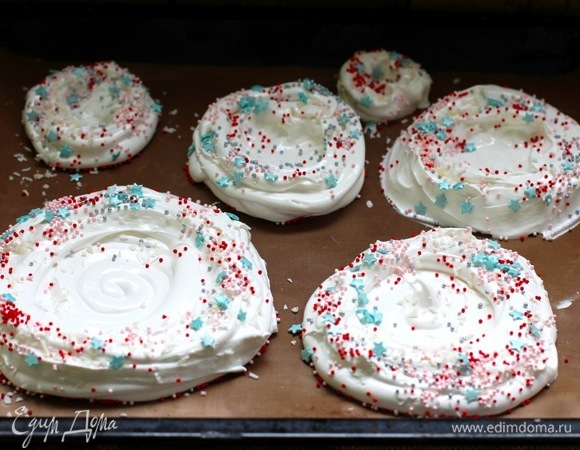 На бумаге для выпечки или силиконовых ковриках заранее сделать разметку из 5 окружностей для уровней елки. Диаметр кругов примерно такой (разброс между слоями примерно 3 см при высоте бортика около 4 см): 19, 16, 13, 9, 6 см. Отсадить ложкой или с помощью мешка безе. Сделать углубления для крема и курда в виде гнезда, бортики можно посыпать кондитерским жемчугом или цветным сахаром. Также посыпаем кокосовой стружкой по желанию Сушить безе 2 ч. Вынуть, охладить. Можно положить в сухое место и хранить несколько дней, пока не станете собирать «елку».