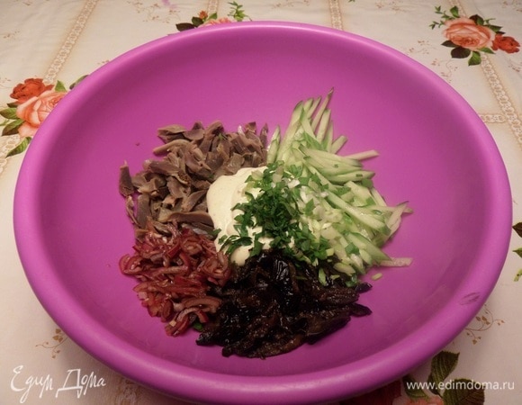 В глубокую чашку выкладываем нарезанные огурцы, чернослив, куриные желудки, маринованный лук. Добавляем приготовленную заправку и зелень.