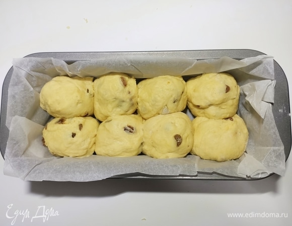 Рабочую поверхность припылить мукой. Разделить тесто на восемь равных частей. Каждую часть вымесить и сформировать из нее шар. Прямоугольную форму для кексов размером 25 х 10 см застелить пергаментной бумагой. Выложить тесто. Накрыть и дать постоять еще 30–40 минут.