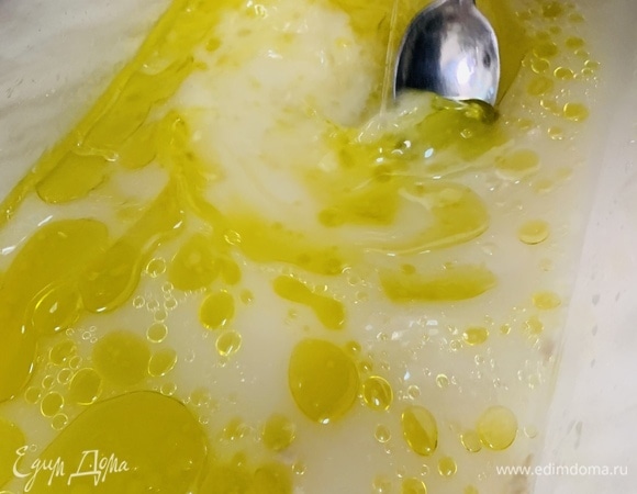 Понадобится восьмилитровый пластиковый контейнер с плотно закрывающейся крышкой. В контейнер наливаем 800 мл воды комнатной температуры. Добавляем дрожжи. Слегка перемешиваем. Вливаем 110 г оливкового масла. Перемешиваем ложкой.