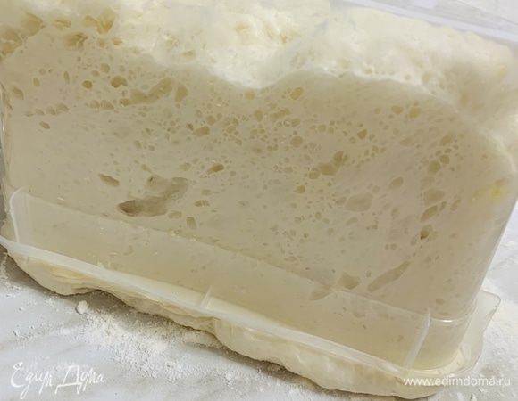 Через 8 часов достаем контейнер с тестом из холодильника. Посыпаем рабочую поверхность мукой и аккуратно переворачиваем на нее контейнер с тестом. Тесто медленно отлипнет от стенок контейнера. Если отходит сложно, тогда можно слегка приподнять контейнер, и тесто спокойно выпадет на стол.