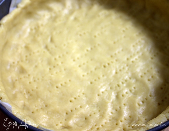 Часть теста отрезать для украшения сверху, остальное распределить по форме с бортиками, застелив ее изначально пергаментом. Дно наколоть вилкой. Убираем в холодильник.