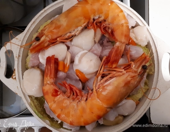 Откройте кастрюлю. Выложите на капусту нарезанное на кусочки рыбное филе, очищенные морские гребешки и креветки. Закройте фольгой и крышкой сверху и оставьте еще на 20 минут.